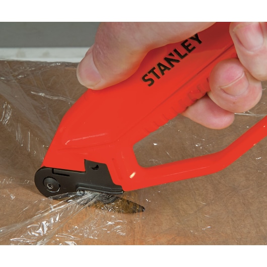 STANLEY 0-10-245 safety knife cutting film wrap on cardboard, close-up side angle.