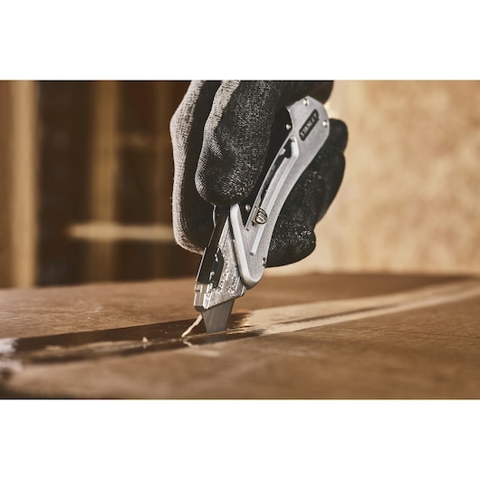 STANLEY 0-10-810 utility knife cutting cardboard, close-up with gloved hand, product photography.