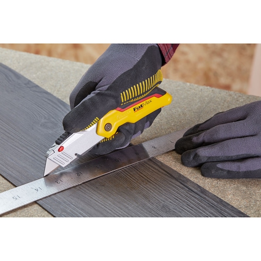 STANLEY 0-10-825 FatMax utility knife in hand cutting vinyl plank along ruler, close-up, photography.