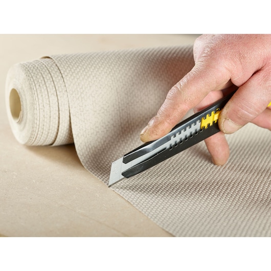 Photo of STANLEY 0-11-301 utility knife cutting textured material roll, close-up, product photography.