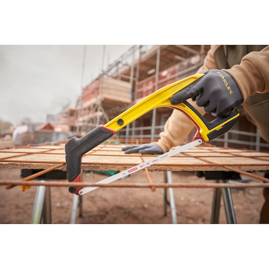 STANLEY 0-20-108 hacksaw with yellow and black handle cutting metal rebar at construction site, side angle.