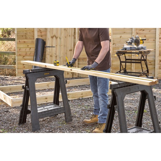 Photo of STANLEY 0-30-657 plastic sawhorses used outdoors for measuring wood in a construction setting.