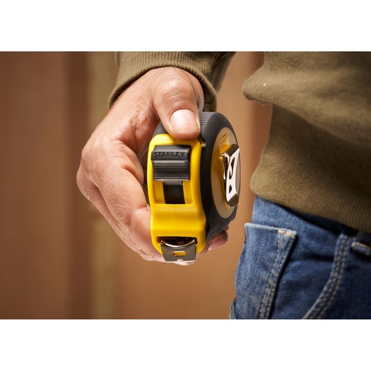 STANLEY 0-30-657 tape measure held in hand near jeans pocket, yellow and black casing.