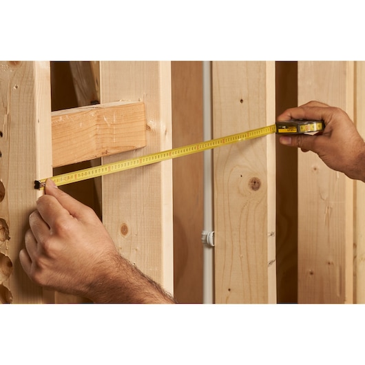 STANLEY 0-32-125 tape measure measuring wooden framing, close-up photo of product in use.