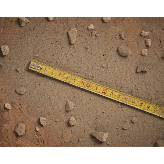 STANLEY 0-32-189 yellow tape measure on dusty ground with scattered rocks, top view photography.