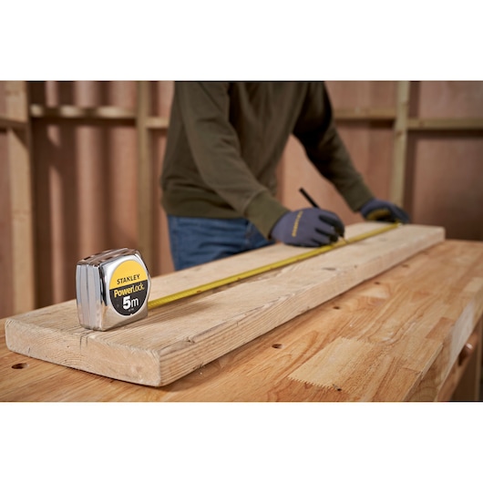 STANLEY 0-33-195 tape measure on wood plank, person marking measurements in workshop setting.