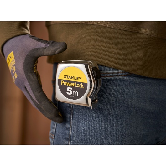 STANLEY 0-33-195 PowerLock tape measure clipped to a jeans pocket, worker with gloves.