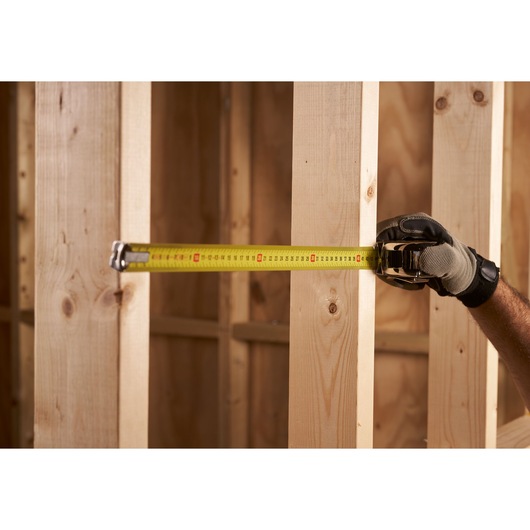 STANLEY 0-33-514 tape measure extended between wooden studs, close-up view, held by gloved hand.