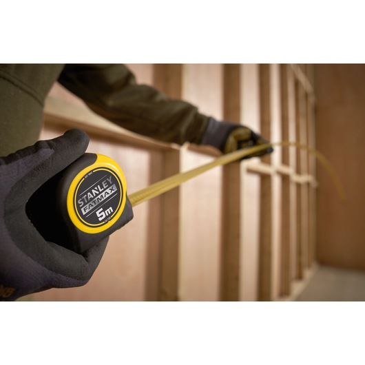 Photo of STANLEY 0-33-720 tape measure, yellow and black, being used to measure wood framing.