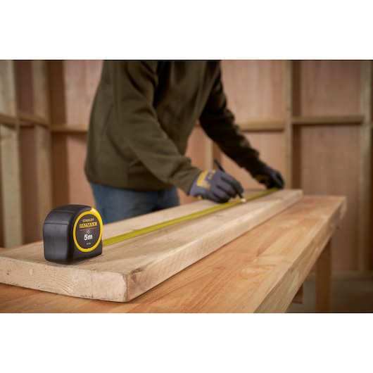 STANLEY 0-33-720 tape measure on wooden board, person marking measurement in workshop setting.