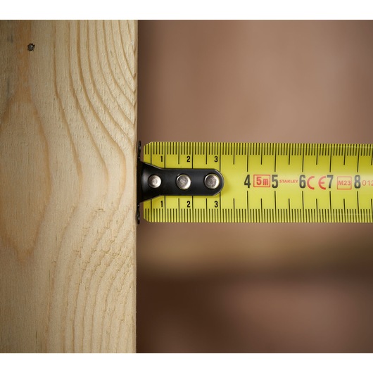 STANLEY 0-33-720 tape measure yellow blade measuring wooden plank, close-up side angle.