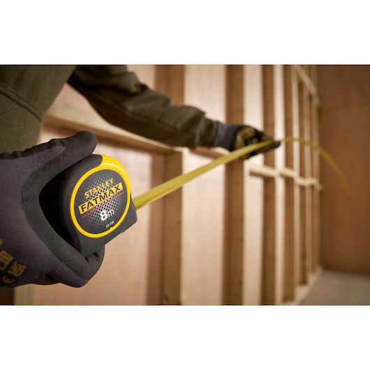 STANLEY FATMAX 8m tape measure SKU 0-33-728 being used to measure wooden studs, perspective close-up.