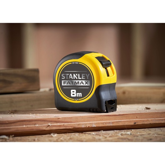 STANLEY 0-33-728 tape measure FATMAX 8m, yellow and black, side view, on wooden surface.