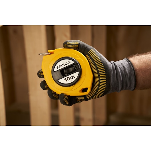 Photo of STANLEY 0-34-102 yellow 10m tape measure held in a gloved hand, construction background.