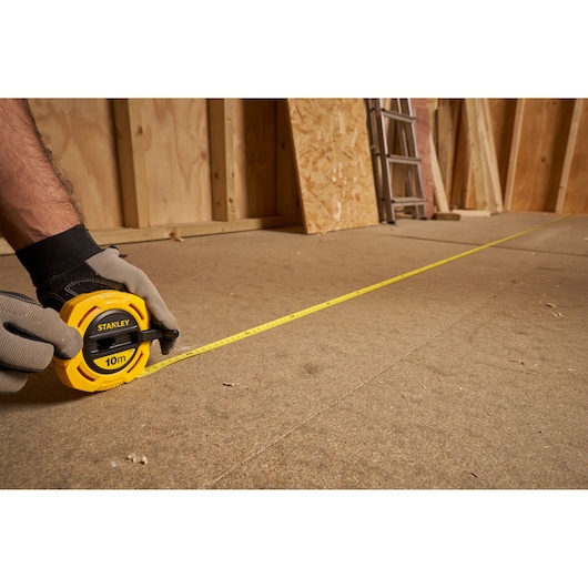 Photo of STANLEY 0-34-295 yellow tape measure extended across a construction floor, held by gloved hands.