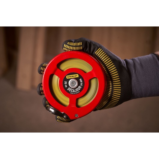 STANLEY 0-34-406 measuring tape with red case and yellow tape, held in a gloved hand, close-up view.