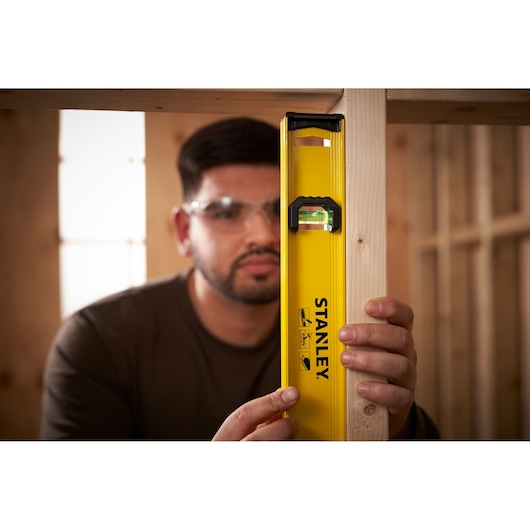 Stanley 0-42-074 yellow spirit level held vertically against wooden beam in workshop.