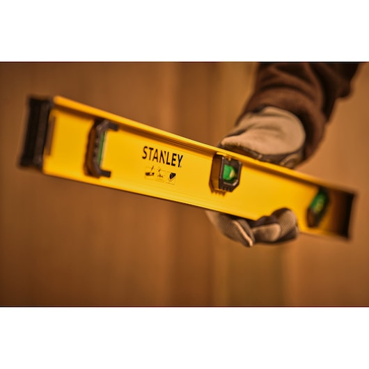 STANLEY 0-42-074 yellow spirit level held by gloved hand, photography close-up at an angle.