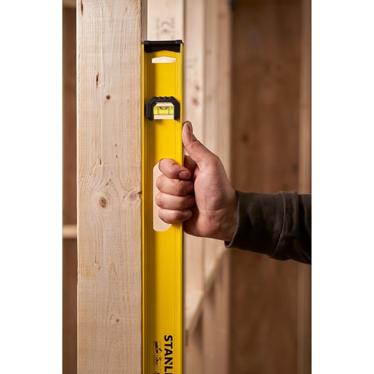 STANLEY 0-42-076 yellow spirit level held vertically against wooden beam, close-up photography.