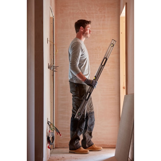 Photo of person holding STANLEY 0-43-648 spirit level tool in a construction area.