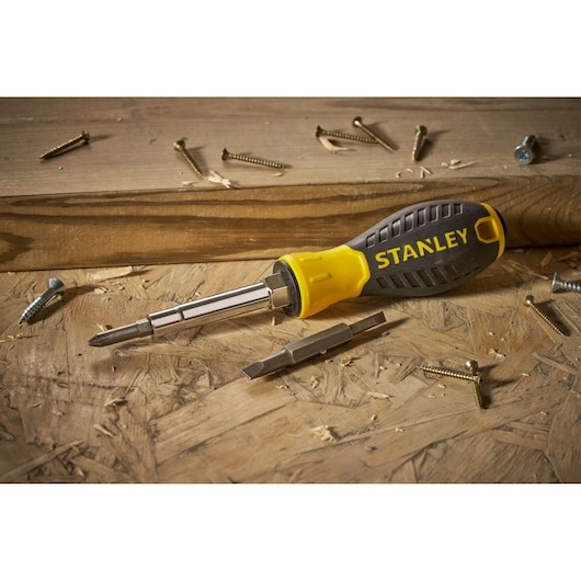 STANLEY 0-68-012 multi-bit screwdriver with yellow and black handle on wood, surrounded by screws.