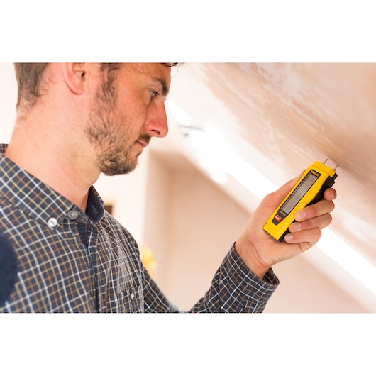STANLEY 0-77-030 moisture meter used by person against wall, yellow handheld tool, product in use.