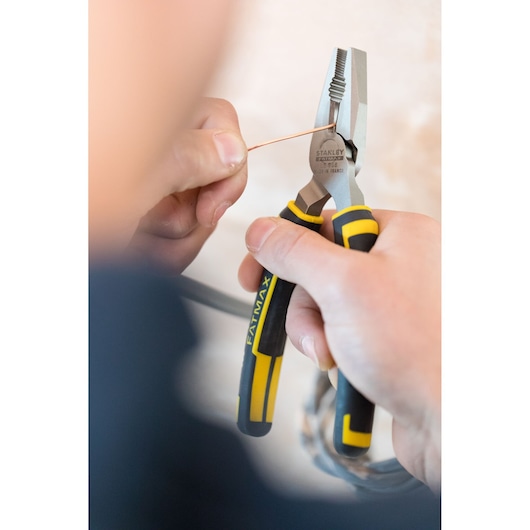 STANLEY 0-89-866 pliers with black and yellow handles gripping copper wire, close-up in hand.