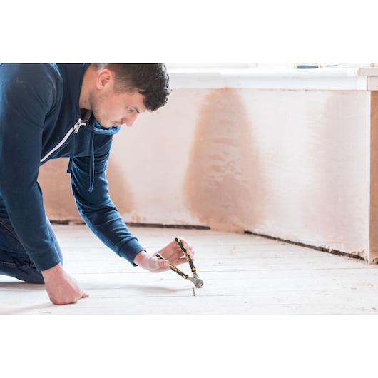 STANLEY 0-89-875 pliers in use pulling a nail from a wooden floor in a home renovation setting.