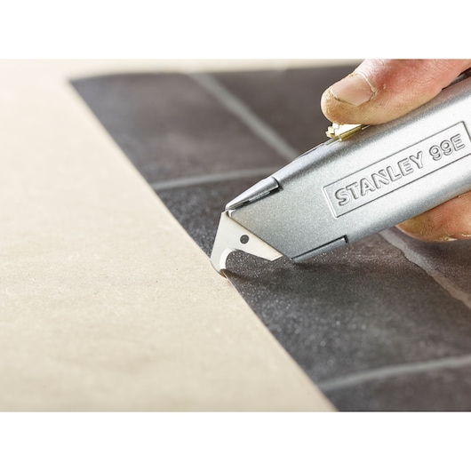 STANLEY 1-11-802 utility knife cutting black material, close-up of curved blade edge and hand holding tool.