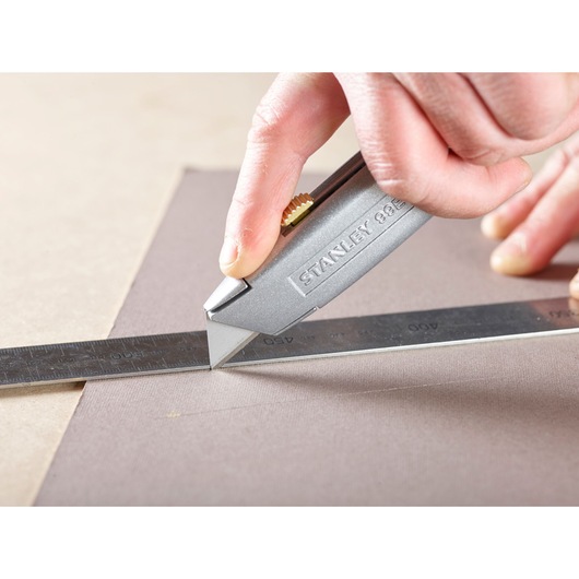 Photo of STANLEY 1-11-911 utility knife cutting material with a metal ruler for alignment.