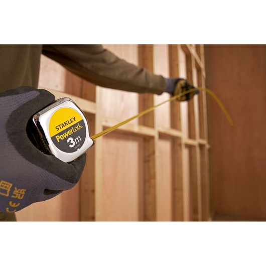Stanley PowerLock 3m tape measure SKU 1-33-238 in use by gloved hand at construction site.