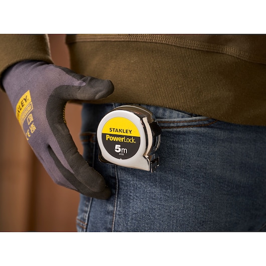 Stanley 1-33-552 PowerLock 5m tape measure clipped to jeans pocket, held by gloved hand.