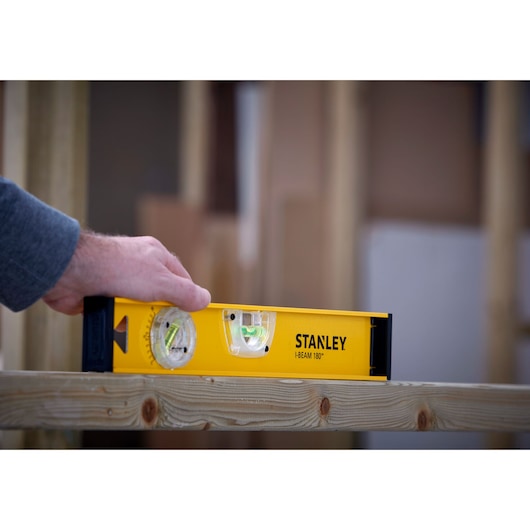 STANLEY 1-42-919 spirit level used to check level on wooden beam, close-up view.