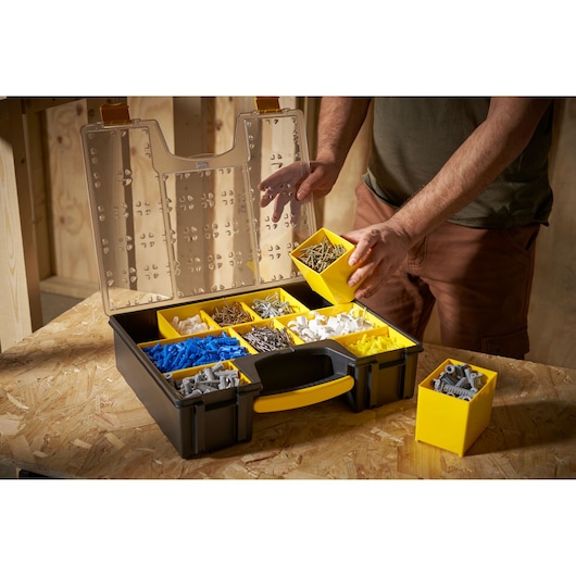 STANLEY 1-92-749 organizer box with yellow removable compartments, filled with assorted screws and wall plugs, on a workbench.