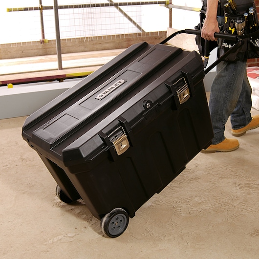 STANLEY 1-93-278 rolling black tool box with metal latches, pulled by a worker at a construction site.