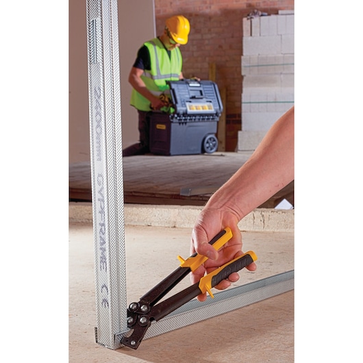 Photo of STANLEY 15-261 aviation snips cutting metal framing at construction site, close-up angle.