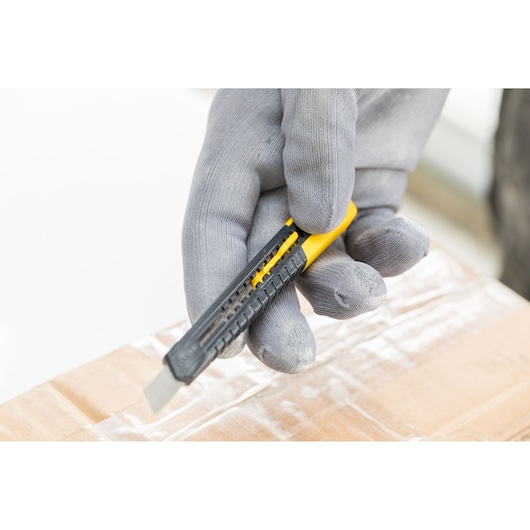 Photo of STANLEY 2-10-150 utility knife cutting tape on a cardboard box, held by a gloved hand.