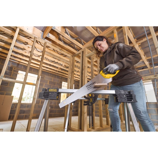 Photo of STANLEY 2-15-244 hand saw with yellow handle in use at a construction site, cutting wood on a sawhorse.