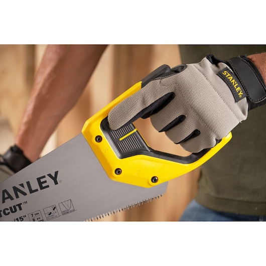 STANLEY 2-15-281 hand saw with yellow and black handle held by gloved hand, close-up angle.