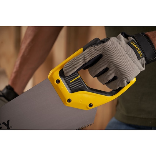 Photo of STANLEY 2-15-289 hand saw with yellow and black handle, gripped by a gloved hand, close-up view.