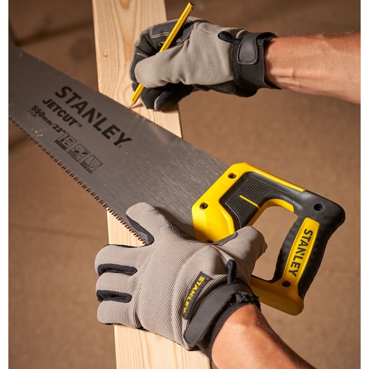 STANLEY 2-15-289 hand saw with yellow and black handle cutting wood, worker wearing gray gloves, close-up.