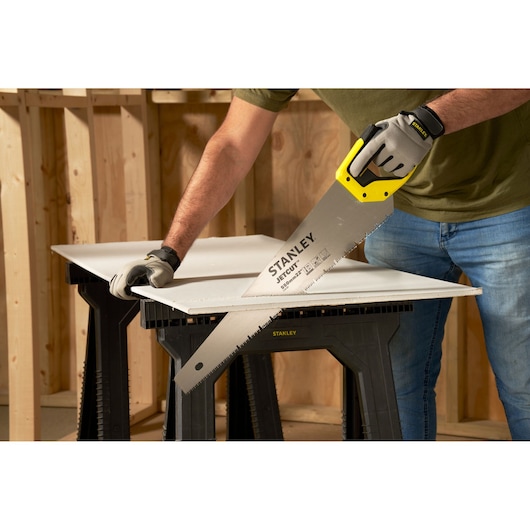 STANLEY 2-20-037 hand saw with yellow handle cutting drywall on black sawhorse, side angle.