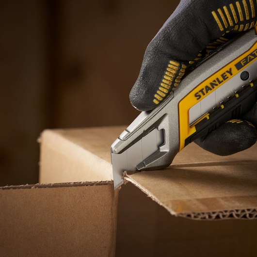 STANLEY 3-11-718 utility knife cutting cardboard, close-up view with gloved hand holding the knife.