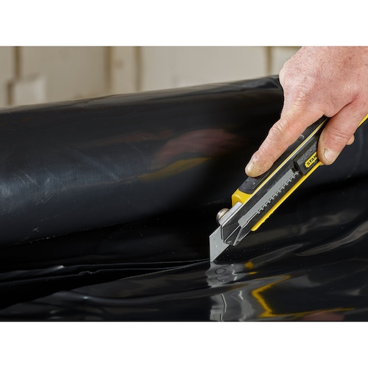 STANLEY 3-11-725 utility knife cutting black plastic sheet, close-up photography.