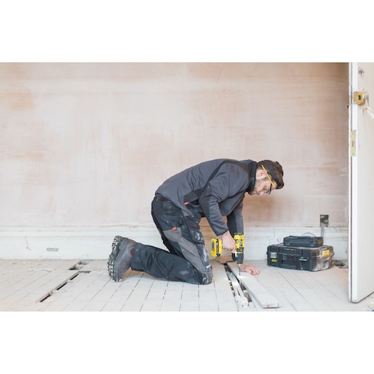 STANLEY FMC626D2K cordless drill used in construction, worker drilling on wooden floor, tool case beside.