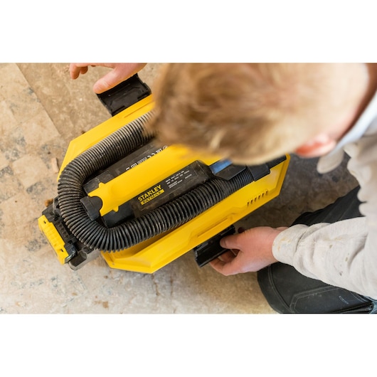 STANLEY FMC795B portable vacuum cleaner with black hose, top view, being handled on a tile floor.