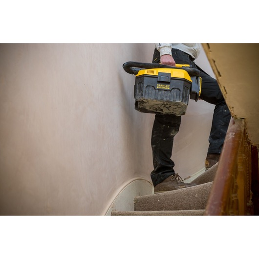 STANLEY FMC795B portable vacuum cleaner in yellow and black carried by a person on stairs, side view.