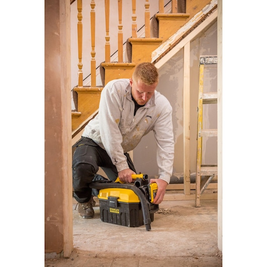 STANLEY FMC795B portable vacuum in use on a construction site floor, worker kneeling during renovation.