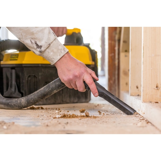 STANLEY FMC795B vacuum cleaner cleaning floor debris, close-up view of hose and nozzle in action