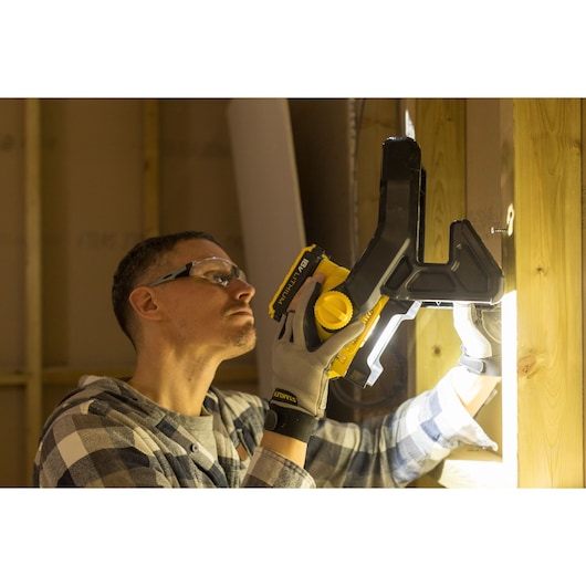 Photo of STANLEY FMCL001B clamp light in use on wooden beam, worker wearing gloves.